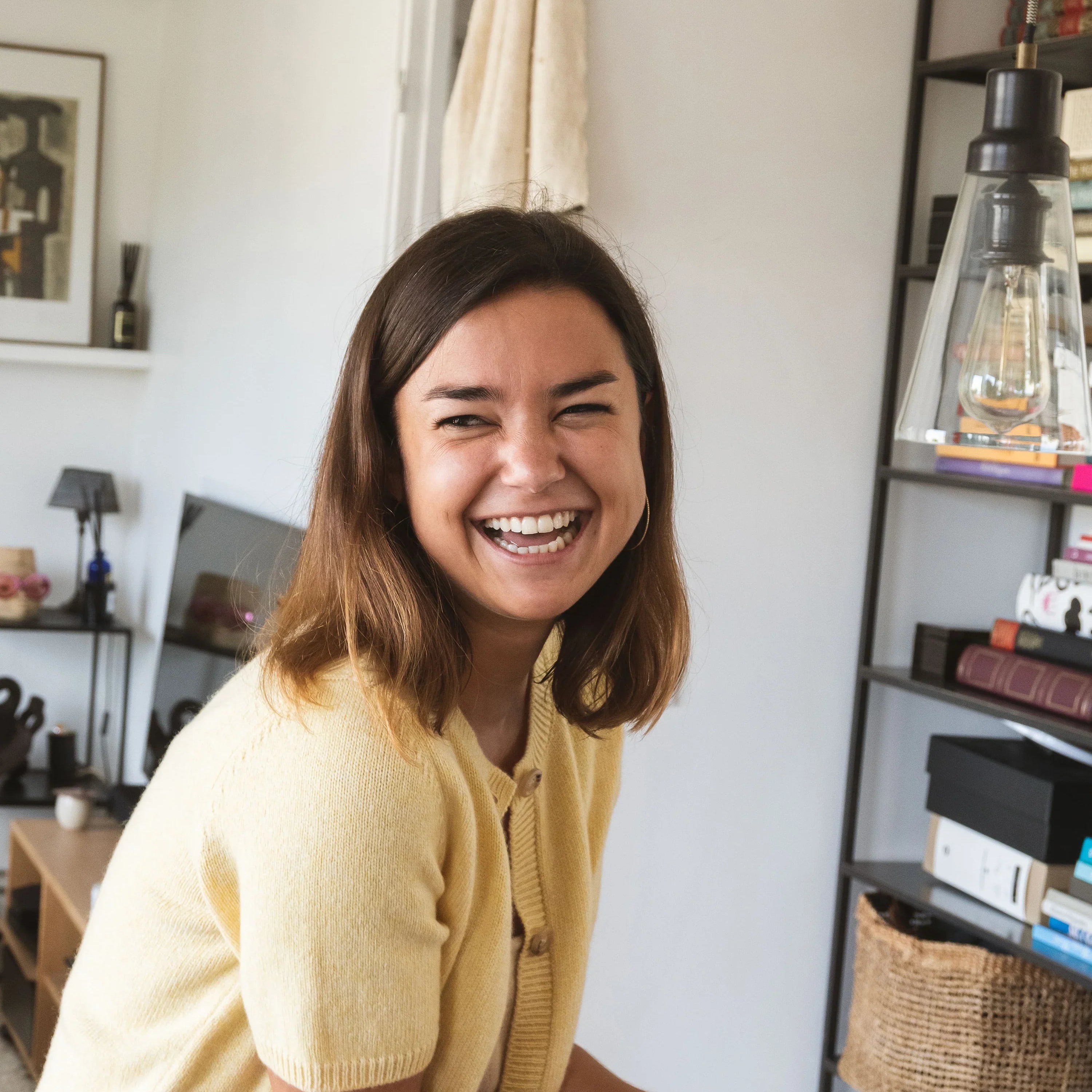 Jessica Troisfontaine wearing Linnea Lund’s Clara cardigan in honey cashmere, smiling warmly while enjoying a Swedish cinnamon roll in her Paris apartment.