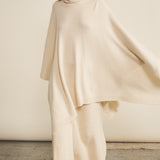 A woman look wearing an oversized white turtleneck cashmere poncho with cut-sides, paired with white pant | Angela | Linnea Lund