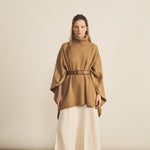 A woman look wearing an oversized camel turtleneck cashmere poncho with cut-sides, paired with white skirt | Angela | Linnea Lund